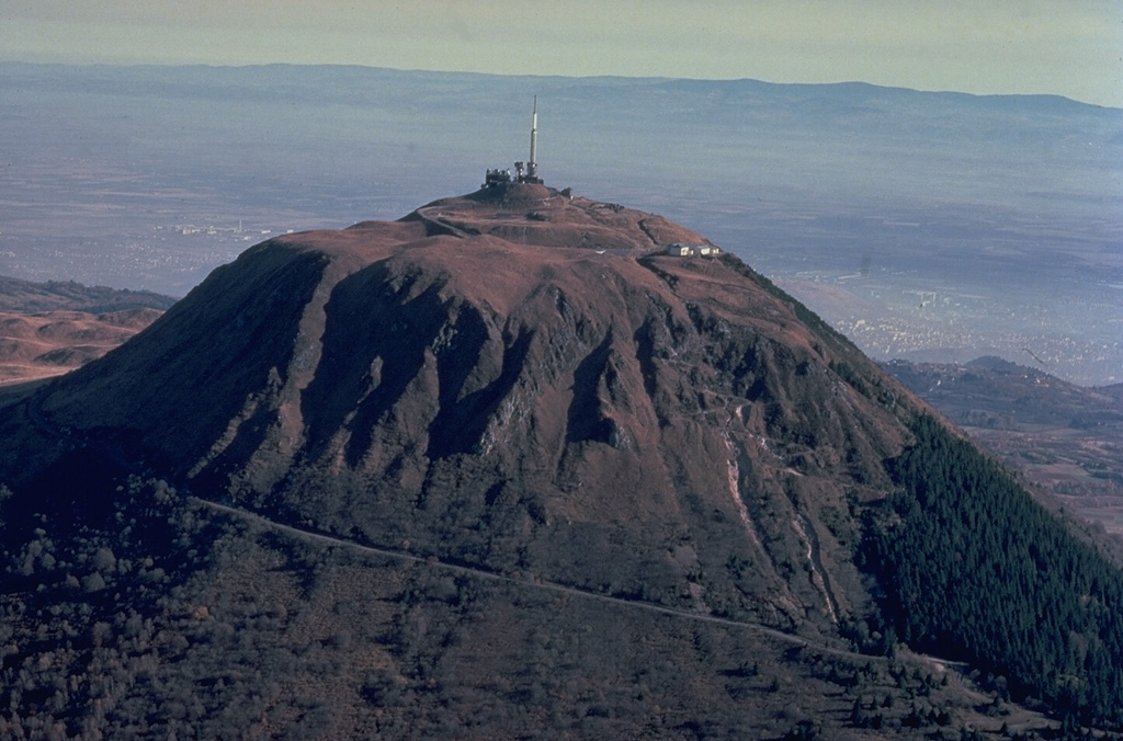 Puy de Dôme (1464 m), the highest peak of the Chaîne des Puys volcanic field, originated during a series of eruptions about 10,000 years ago.  Explosive destruction of the eastern side of a massive lava dome, whose western face is seen in this photo, was followed by growth of a second dome.  Crumbling of a spine capping the second dome formed the low mound of breccia at the summit of Puy de Dôme, which has been covered by a pyroclastic-flow deposit from nearby Killian volcano. Copyrighted photo by Katia and Maurice Krafft, 1978.