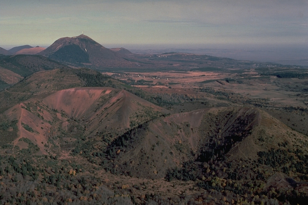 The twin breached cinder cones of Puy de Lassolas (left) and Puy de la Vache (right) were formed during eruptions about 8000 years ago.  The cones were breached when moving lava flows carried away portions of them.  A compound lava flow from the two cones traveled 14 km to the SE.  The high peak in the distance to the north is the Puy de Dôme lava dome. Copyrighted photo by Katia and Maurice Krafft, 1978.