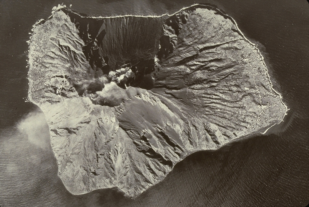 Stromboli is shown in this aerial view with the top of the photo facing NW. It has been continuously active for more than 1,300 years and was constructed in two cycles, the last of which formed the western side of the island. A plume trails to the S from the active vent at the head of the Sciara del Fuoco. The scarp was created by a Pleistocene landslide and channels pyroclastic ejecta and lava flows to the west. Photo by the Italian Air Force.