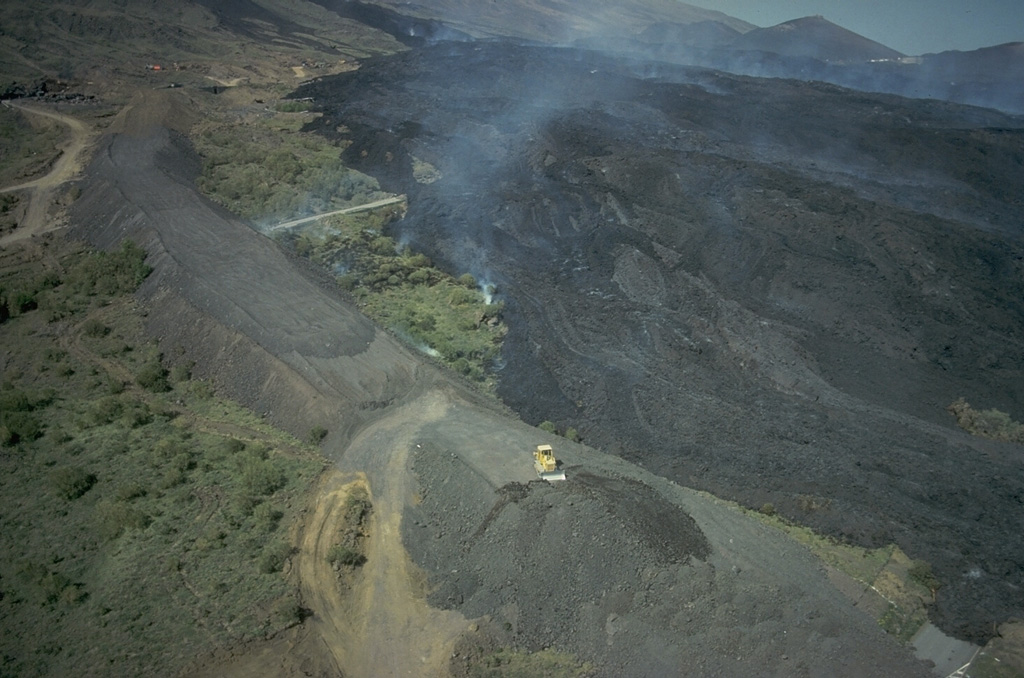 A major S-flank eruption of Etna beginning on 28 March 1983 produced lava flows that damaged tourist facilities. Extensive efforts at lava diversion, such as the gray embankment at the left of this photo, were made to divert the flows from populated areas. The flows eventually descended to 1,080 m altitude and stopped short of several villages. Photo by Romolo Romano, 1983 (IIV-CNR, Catania, Italy).