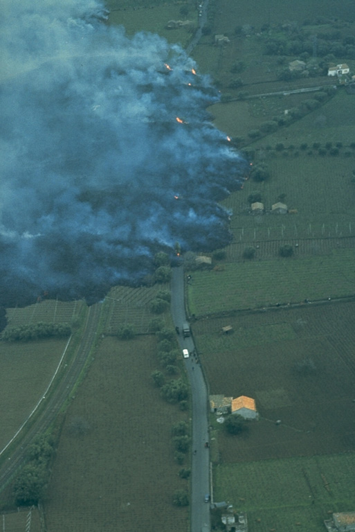 A March 1981 lava flow from vents on the upper NW flank of Mount Etna in Sicily descended 8 km into populated areas and caused extensive damage to orchards and farm buildings. This photo shows the steaming lava flow front as it overran a railroad bed and highway. Photo by Romolo Romano, 1981 (IIV-CNR, Catania, Italy).