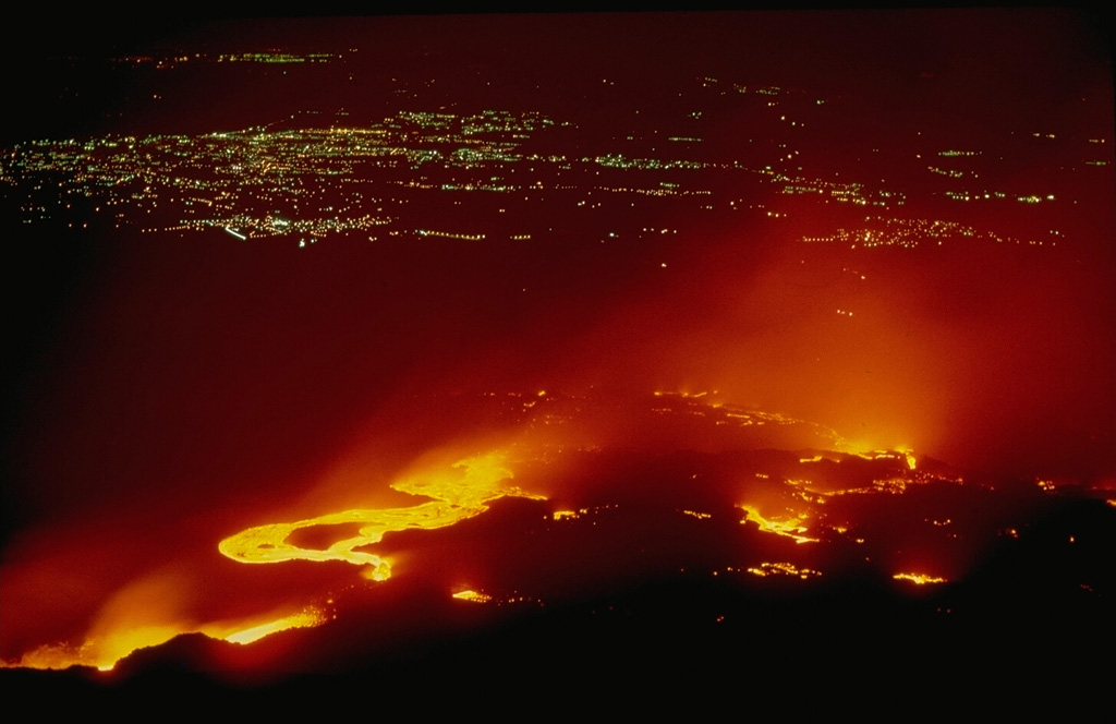 Incandescent lava flows in May 1983 descend the south flank of Mount Etna toward city lights.  During the four-month-long eruption, lava descended to 1080 m altitude, stopping just short of inhabited areas.  Extensive efforts were made to construct barriers to divert lavas away from populated areas.  Copyrighted photo by Katia and Maurice Krafft.