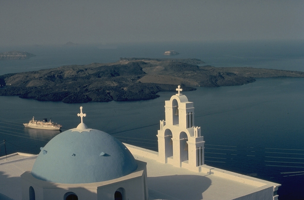 A volcanic cone forms low islands within the largely submerged, 7.5 x 11 km caldera of Santorini (Thera), as viewed from the town of Firá, on the east rim of the caldera.  Santorini volcano consists of four partially overlapping calderas, the youngest of which was produced by a major eruption during the Minoan period about 3500 years ago. The Akrotíri Peninsula (upper right) and the small island in the middle distance are parts of the opposite caldera wall.  Eruptions from the post-caldera cone have been recorded from 197 BCE until 1950. Copyrighted photo by Katia and Maurice Krafft, 1989.