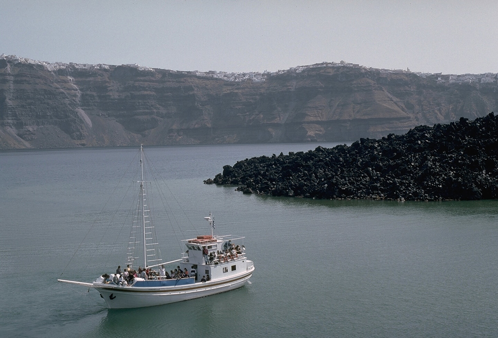 The dacitic lava flow at the right is part of the Dafni lavas, erupted early in the course of an eruption that lasted from 1925 to 1926. Like many other of Santorini's post-caldera eruptions, this eruption began with submarine explosions and lava extrusion. Explosive activity produced eruption plumes up to 3.2 km high. The east wall of Santorini caldera hosts the town of Firá across the caldera bay. Photo by Lee Siebert, 1994 (Smithsonian Institution).