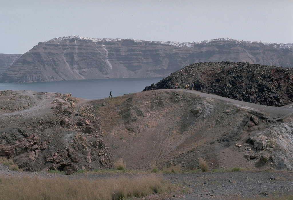 The dark-colored lava flow at the right center of the photo, and the crater in the foreground, were formed during an eruption from 1939 to 1941. The lava flows traveled to the E and W, reaching almost to the sea on the E side and extending into the caldera bay at several locations on the W side on Nea Kameni island. A chain of N-S-trending craters was formed during the eruption. The crater seen in this photo cut lava flows of an earlier 1866-1870 eruption.  Photo by Lee Siebert, 1994 (Smithsonian Institution).