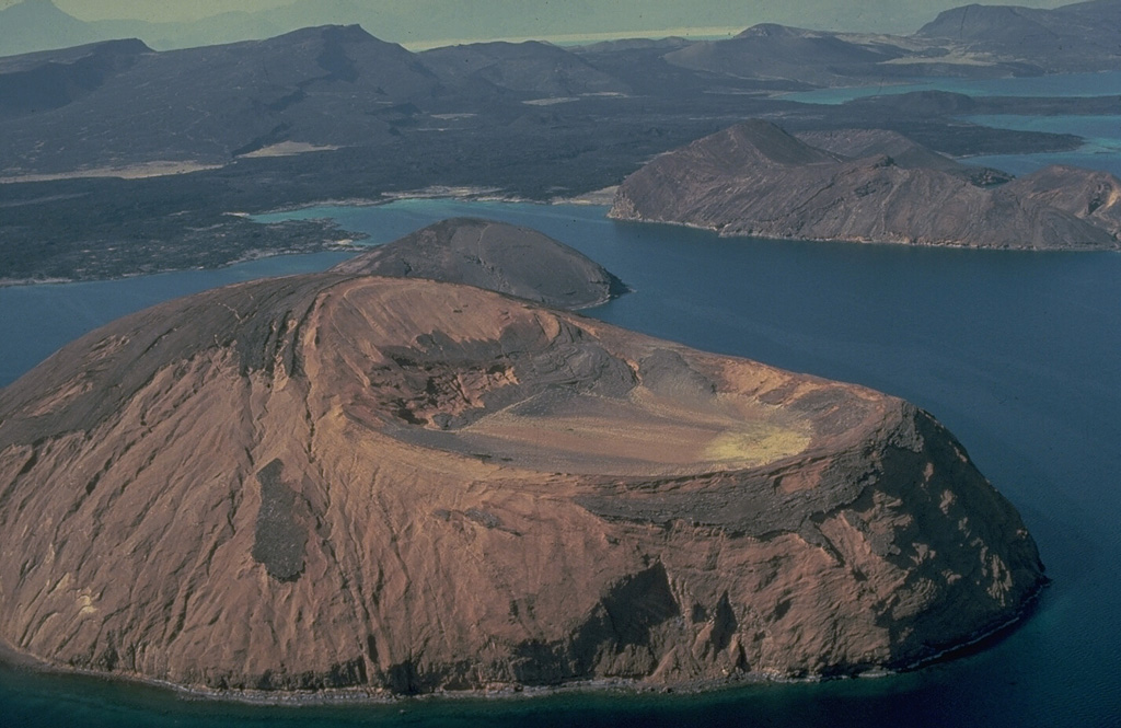 The three tuff cones of Kodda Ginni Koma (foreground), Ounda Ginna Koma (the small island in the center), and Baddi Koma (upper right) were formed when rising magma along the Ardoukoba Rift encountered waters of the Ghoubbat al Kharab gulf of the Red Sea.  Fresh lava flows in the background were erupted from the parallel NW-SE-trending fissures of Ardoukôba volcano in the country of Djibouti.  Tilted fault blocks in the background dip to the SW and NE, away from the center of the rift valley. Copyrighted photo by Katia and Maurice Krafft, 1976.