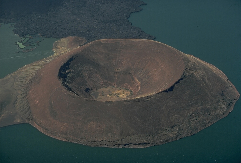 The pristine Naboiyoton tuff cone rises above Lake Turkana in northern Kenya.  The tuff cone, seen here from the north, is a satellitic cone on the north flank of The Barrier volcano.  It rises 180 m above the lake, and was formed by explosive eruptions produced when magma rising up along the East African Rift encountered the waters of Lake Turkana.  The age of the tuff cone is not known, but its lower slopes lack erosional terraces created during higher stands of the lake.  The lava flow at the top was erupted from The Barrier volcano. Copyrighted photo by Katia and Maurice Krafft, 1977.