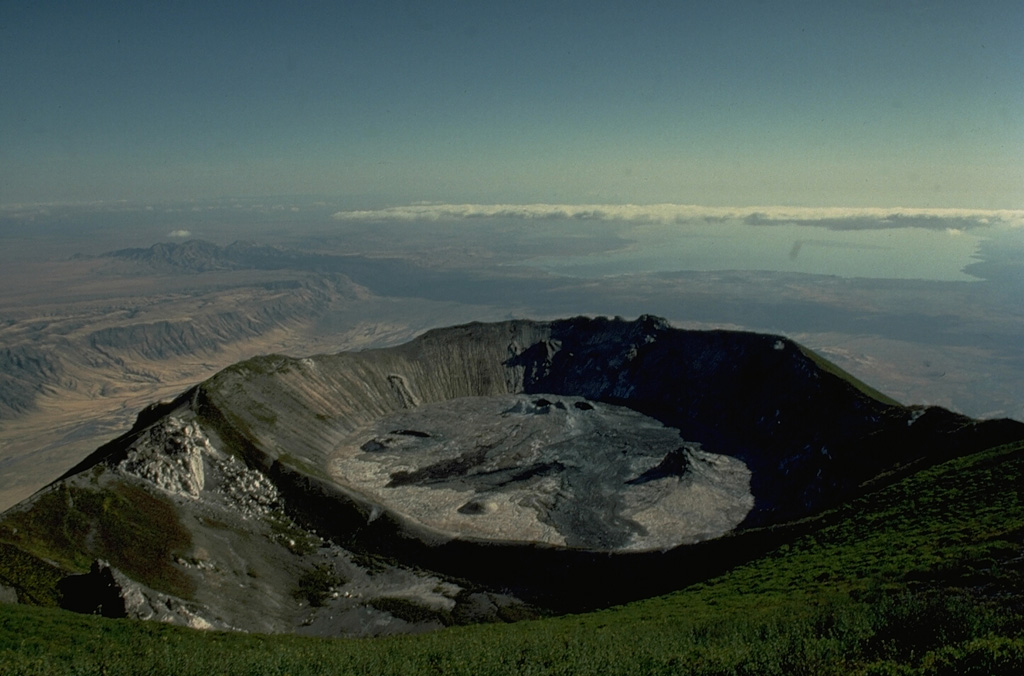 The northern crater of Ol Doinyo Lengai is seen here from the summit of the volcano in 1988 with Lake Natron in the distance.  Ol Doinyo Lengai was built on the floor of the East African Rift, whose western wall forms the escarpment at the left.  Newly erupted lava flows darken the floor of the crater in this photo taken during the course of a decade-long eruption that began in 1983. Copyrighted photo by Katia and Maurice Krafft, 1988.