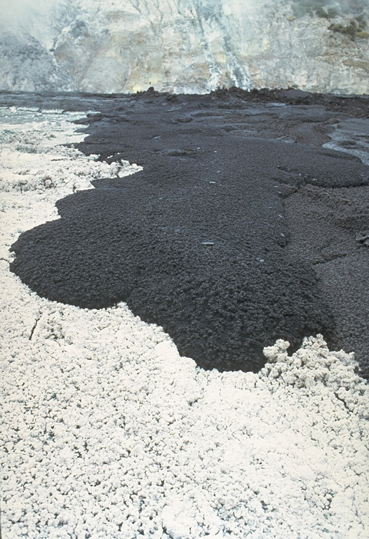 A black lava flow advances across the floor of Tanzania's Ol Doinyo Lengai volcano on June 27, 1988.  The white-colored area in the foreground is not covered with snow, but is the surface of a recently cooled lava flow.  The unusual carbonatitic (sodium carbonate) chemistry of flows from this volcano produces lava flows that are initially black, but have white edges within a few hours and alter to an entirely white surface within 48 hours. Copyrighted photo by Katia and Maurice Krafft, 1988.