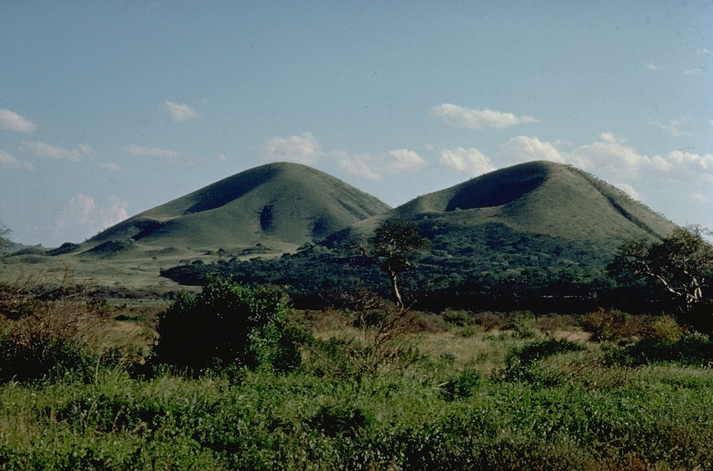The 100-km-long NW-SE-trending Chyulu Hills volcanic field, located 150 km east of the Kenya Rift, contains several hundred small cinder cones and lava flows.  Many are Holocene in age, including two that erupted during the mid-19th century.  Volcanic activity began about 1.4 million years ago with eruptions in the northern Chyulu Hills and migrated to the SE, where most of the younger cones are found. Copyrighted photo by Katia and Maurice Krafft, 1976.