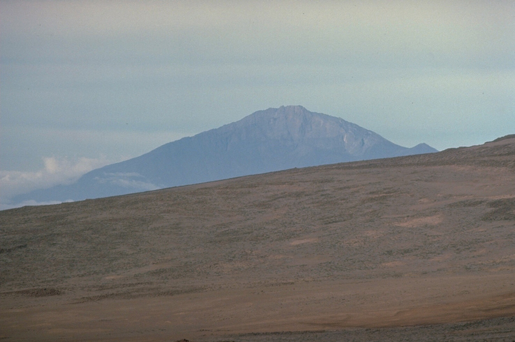 Meru volcano, Africa's fourth highest mountain, rises to the west of its more prominent neighbor, Kilimanjaro.  Seen here from the slopes of Kilimanjaro, 4565-m-high Meru is cut by a 5-km-wide breached caldera on the east side that formed about 7800 years ago when the summit of the volcano collapsed.  The resulting massive debris avalanche and lahar traveled as far as the western flank of Kilimanjaro volcano.  The historically active Ash Cone forms a prominent symmetrical cone inside the breached caldera.   Copyrighted photo by Katia and Maurice Krafft, 1977.