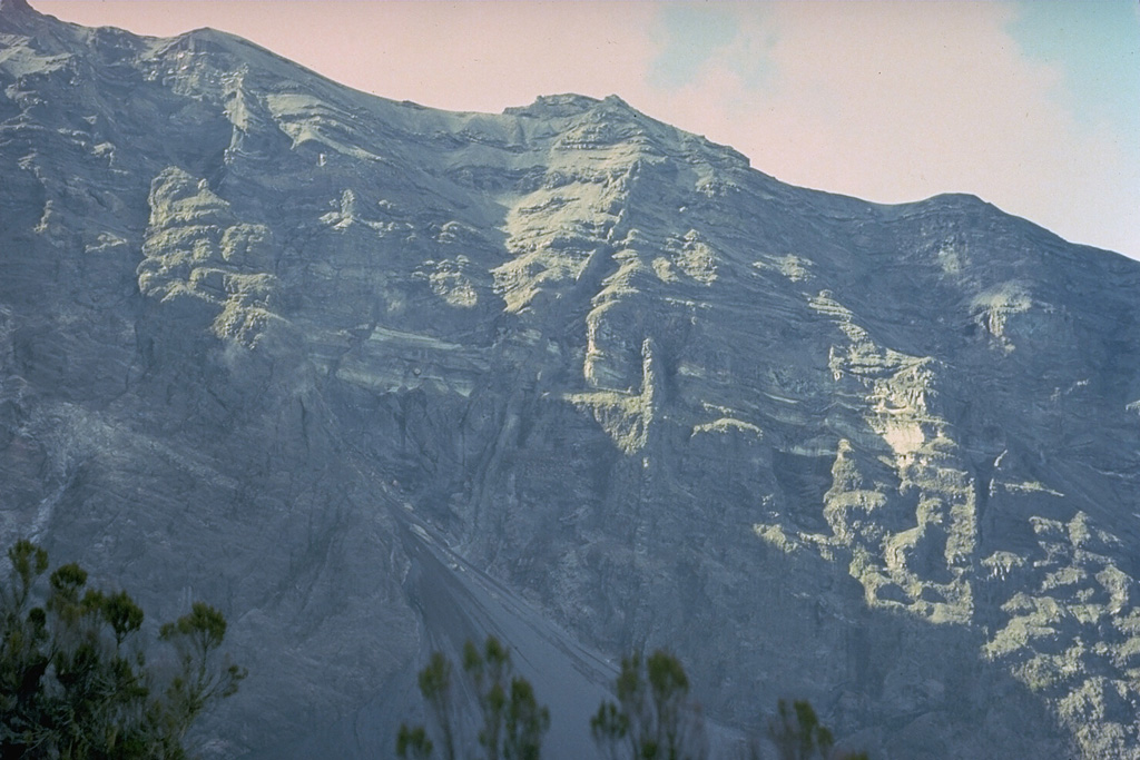 The northern wall of the horseshoe-shaped caldera cutting the summit of Meru volcano rises vertically up to 900 m above the caldera floor.  The 5-km-wide caldera is breached to the east and was formed as a result of a massive volcanic landslide about 7800 years ago. Copyrighted photo by Katia and Maurice Krafft, 1977.