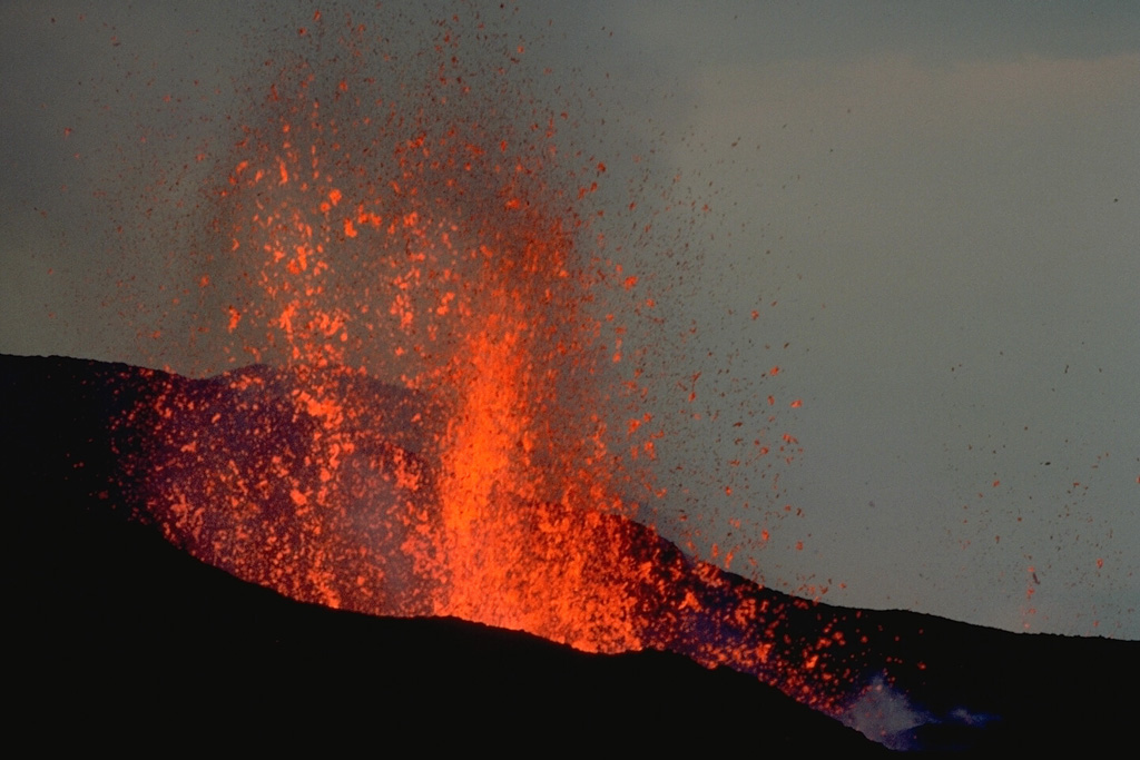 A new cinder cone, named Gasenyi, ejects fragments of incandescent lava in February 1980.  The cone was formed during an eruption that began from a north-flank fissure on January 30.  A 2-km-long fissure ejected scoria and ash and fed lava flows.  In early February lava fountains were localized at the north end of the fissure and built Gasenyi cinder cone. On the 10th, new vents opened at the south flank of the cone.  An explosion the next day destroyed this cone and produced a double-cratered cone.  Copyrighted photo by Katia and Maurice Krafft, 1980.