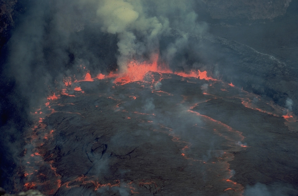 Lava fountains rise along the circular margin of a lava lake in the summit crater of Nyiragongo volcano in June 1973.  Incandescence is visible through fractures in cooled slabs of lava on the surface of the convecting lava lake.  Nyiragongo is renowned for its long-term lava lakes.  A half century of continuous lava-lake activity ended suddenly on January 10, 1977, when the lava lake drained rapidly through flank fissures.  Prior to draining, the lava lake rose to an elevation of 3300 m, its highest recorded level, only 170-m below the crater rim. Copyrighted photo by Katia and Maurice Krafft, 1973.