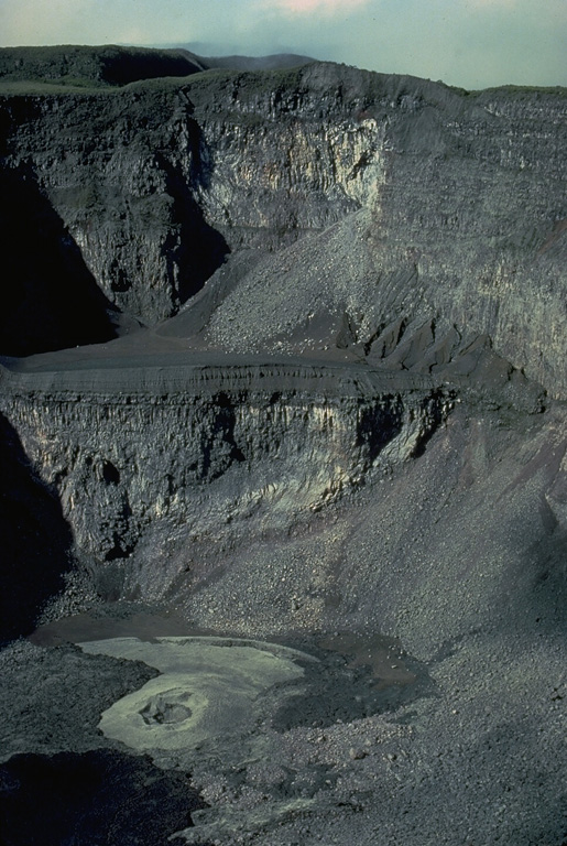 Karthala, the largest of the two shield volcanoes forming Grand Comore Island, contains a compound 3 x 4 km summit caldera.  The strombolian cinder cone on the floor of the steep-walled, 300-m-deep Choungou-Chahale caldera, seen here from the north, is surrounded by lava flows from the 1965 and 1972 eruptions.  Elongated rift zones extend to the NNW and SE from the summit of the volcano.  More than twenty eruptions have been recorded since the 19th century from both summit craters and flank vents. Copyrighted photo by Katia and Maurice Krafft, 1980.