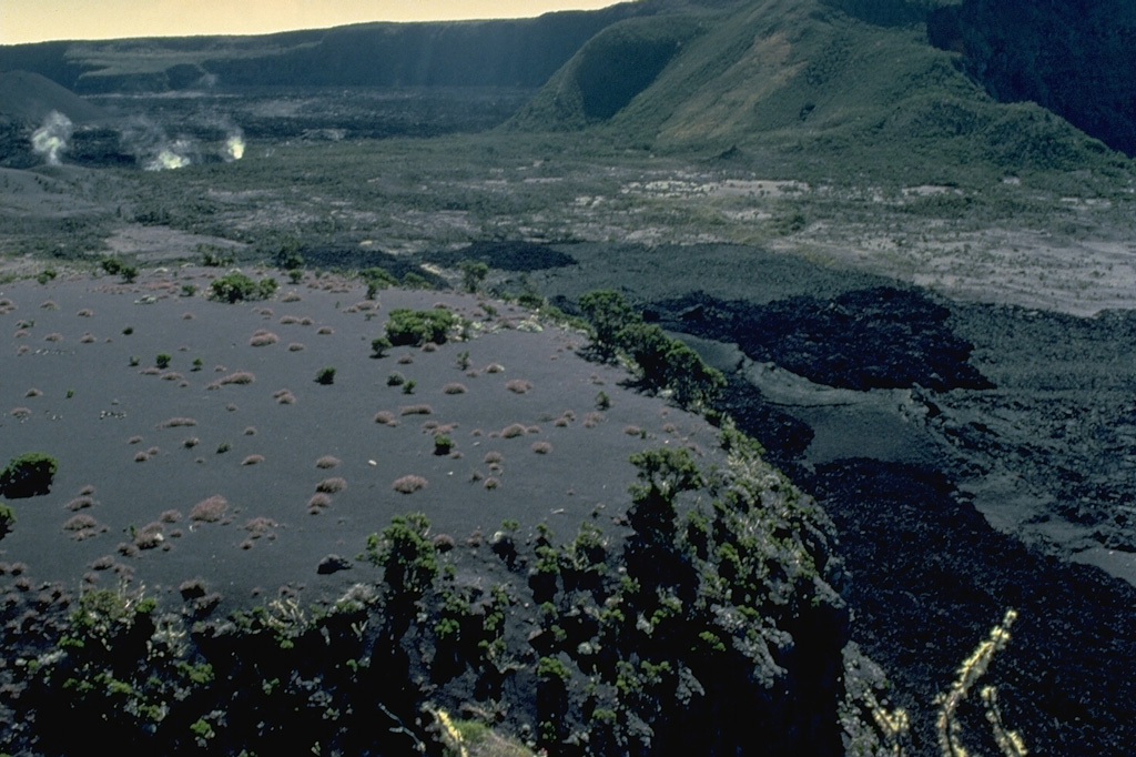 Steam rises from fumaroles at the margins of the Choungou-Chagnoumeni pit crater in the summit caldera of Karthala volcano.  This 1980 view from the SSE shows black lava flows from the 1972 eruption and gray lava flows from the 1965 eruption on the caldera floor at the lower right. Copyrighted photo by Katia and Maurice Krafft, 1980.