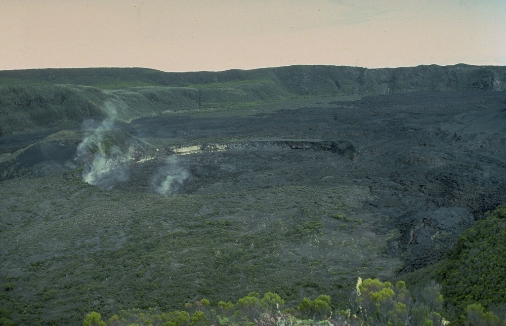 The 250-m-wide Chongou-Chagnoumeni pit crater (center) cuts the northern part of the compound summit caldera of Karthala volcano.  The steaming 30-m-deep pit crater was formed during an eruption in 1918 that also greatly enlarged the Chongou-Chahale pit crater to the south.  Unvegetated lava flows from the 1972 eruption cover the caldera floor behind the pit crater. Copyrighted photo by Katia and Maurice Krafft, 1980.