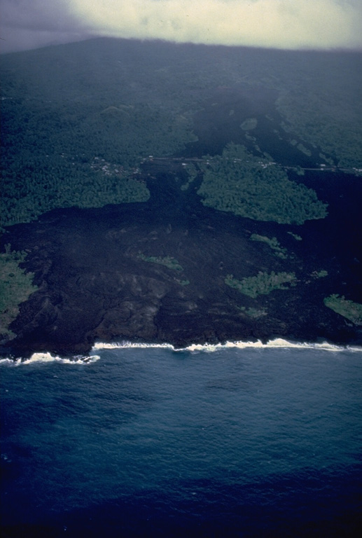 An eruption from a SW-flank fissure beginning April 5, 1977 produced a lava flow that reached the sea and destroyed or damaged villages located along the E-W-trending road cutting across the center of the photo.  The 5-day-long eruption originated from a cinder cone constructed along a vent at 360-m altitude.  The basaltic lava flow traveled about 2 km and reached the sea along a 1.5-km-long front.  About 300 houses were destroyed in the villages of Singani (left) and Hesa (right).  The flow diverged around a vegetated kipuka, sparing houses there. Copyrighted photo by Katia and Maurice Krafft, 1980.