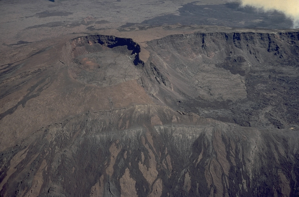 During a six month period beginning in July 1972, eruptions took place from vents on the south, SE, NE, and north sides of the summit lava shield of Piton de la Fournaise.  This aerial view from the south in November 1973 overlooks circular Bory (left center) and oval-shaped Dolomieu (right center) craters.  The unvegetated lava flows in the foreground were erupted from circumferential fissures during the 1972 eruption.  The dark lava flow at the upper right, beyond Bory and Dolomieu craters, also was erupted in 1972. Copyrighted photo by Katia and Maurice Krafft, 1973.