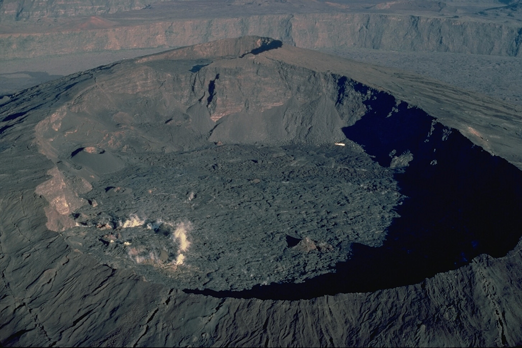 Dolomieu crater, seen here from the east in 1987, forms the principal summit crater of Piton de la Fournaise volcano.  The western wall of Dolomieu crater cuts the rim of the smaller Bory Crater.  Dolomieu crater, whose form has varied widely during the course of historical eruptions, dates back to July 1791.  Twentieth-century lava flows cover the floor of the crater.  The western wall of the most recent caldera of Piton de la Fournaise is visible in the distance. Copyrighted photo by Katia and Maurice Krafft, 1987.