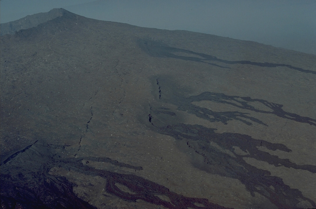 A series of en echelon fissures cutting the upper NE flank of the central lava shield of Piton de la Fournaise volcano fed these black, unvegetated lava flows that descend the flanks of the volcano.  Most of the eruptions of Piton de la Fournaise, one the world's most active volcanoes, originate from fissure vents.  Circumferential fissures such as these occur near the crater rim; more commonly radial fissures extend down the flanks perpendicular to the summit crater rim. Copyrighted photo by Katia and Maurice Krafft, 1976.