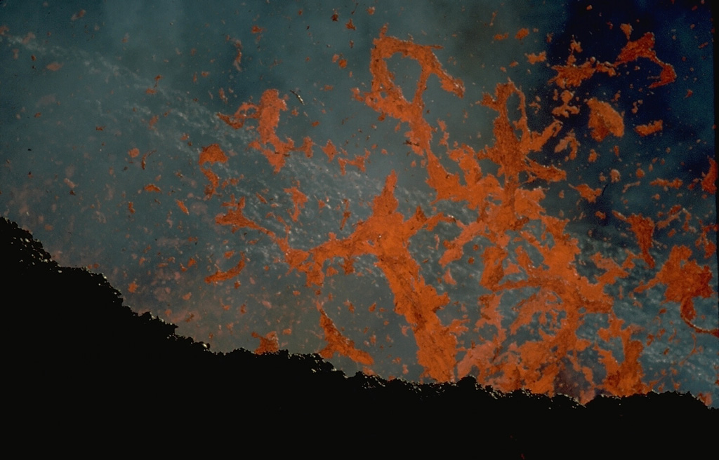 Incandescent spatter rises above a vent in January 1984.  Effusive and explosive eruptions took place December 4, 1983-January 18, 1984 and January 18-February 18, 1984 from fissure vents 400 m apart on the SSW flank of the central lava shield of Piton de la Fournaise.  Two cinder cones formed above the vents, located at 2200-m altitude.  They produced lava flows that traveled down the SE flank. Copyrighted photo by Katia and Maurice Krafft, 1984.