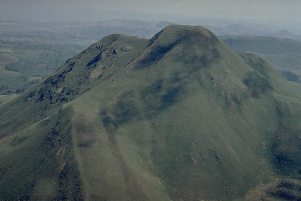 This vegetated lava dome is one of many at the Itasy volcanic field in central Madagascar.  A steep-sided viscous lava flow descends to the left of the summit.  Lateral levees at the margins of the flow form the distinct ridges at the lower left below a sharp bend in the lava flow. Copyrighted photo by Katia and Maurice Krafft, 1973.