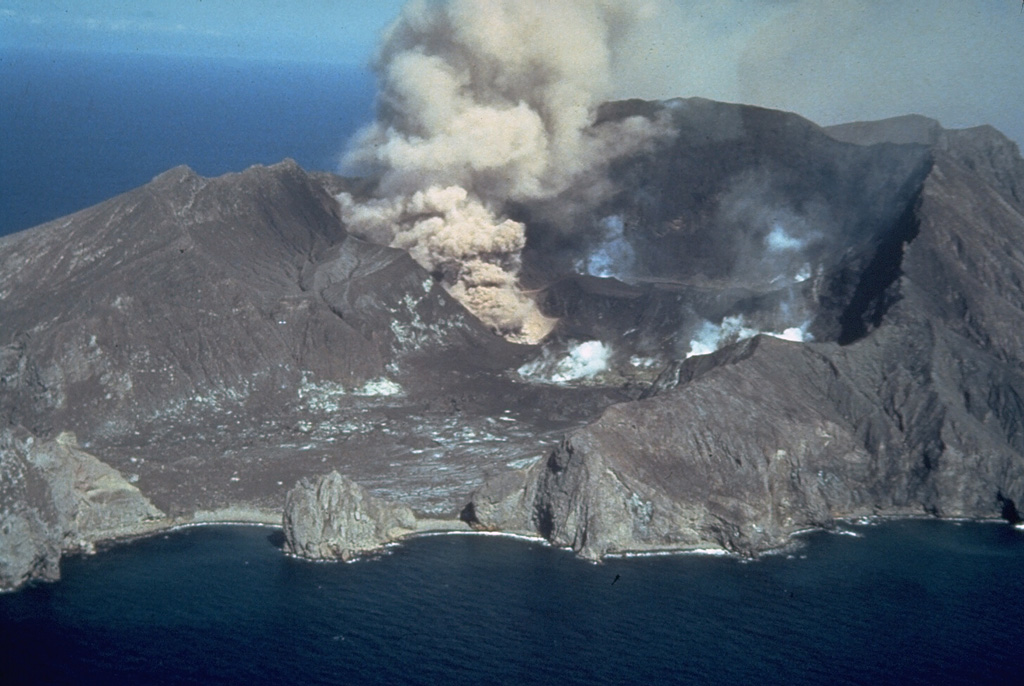 An eruption from White Island (also called Whakaari) on 12 February 1977 is viewed from off the NE coast. The ash plume originates from the Christmas Crater vent, formed the previous year, shortly after the start of the eruption on 18 December. The first 20th century eruption to produce new magmatic material took place a month after the date of this photo. Intermittent phreatomagmatic eruptions continued until late 1981. Photo by Simon Nathan, 1977 (New Zealand Geological Survey).