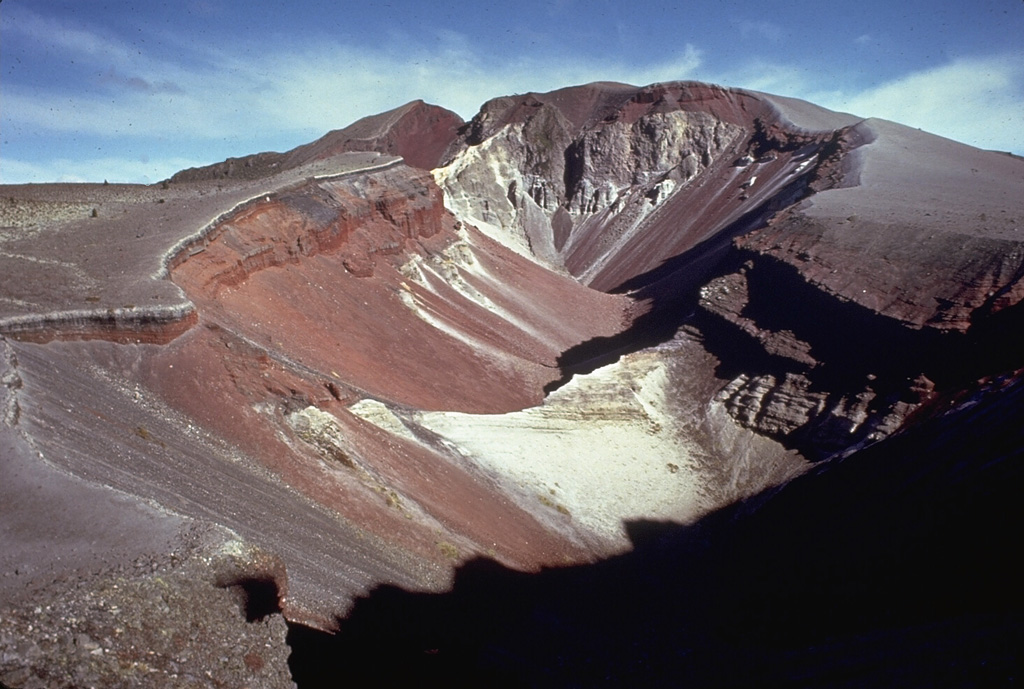 The 1886 Tarawera eruptive fissure, seen from the N, formed across lava domes of the 800-year-old Kaharoa eruption. The red and black rocks of the 1886 eruption, 20-30 m thick here, overlie white rhyolitic Kaharoa eruption deposits. This view shows a 2-km-long section of the 8-km en-echelon fissure with gray rocks of the Ruawahia lava dome appearing at the far end. Photo by Bruce Houghton (Wairakei Research Center).