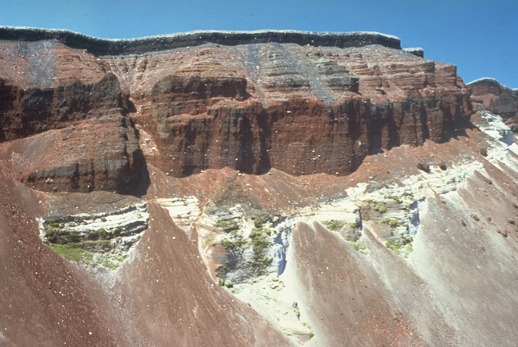 The SE part of the fissure within Ruawahia crater reveals stratigraphy from the circa 700 BP Kaharoa and 1886 CE eruptions. The 35-m-thick light-colored Kaharoa Plinian deposits at the base are largely obscured by talus fans of scoria from above. The thick overlying bright red scoria is from phase 2 of the 1886 eruption. Above it is a thin black zone (phase 3) consisting of very widespread scoria. Phase 4 (at the top) consists of white rhyolitic blocks ripped off the walls during the vent widening in the last half hour of the 10 June 1886 eruption. Photo by Bruce Houghton (Wairakei Research Center).