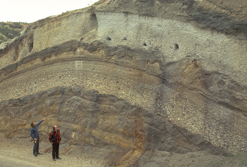 Volcanologists Colin Wilson and Peter Ballance examine a roadcut that dissects deposits of major eruptions from the Taupo volcanic center. The bottom visible unit is an exposure of an unwelded pyroclastic flow deposit from the Oruanui eruption, which formed Taupo's initial caldera about 22,600 years ago. Light-colored pumice fall deposits from other major eruptions are between it and the deposits of the 1,800-year-old Taupo eruption (upper right), which were responsible for Taupo's second caldera. Photo by Bruce Houghton (Wairakei Research Center).