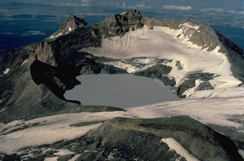 Crater Lake, at the summit of Ruapehu volcano, has produced frequent phreatic explosions during historical time.  The depth of the 600-m-wide crater has varied dramatically in recent years, with the maximum depth ranging from 0 to 300 m. Occasionally the lake has been completely drained by explosive eruptions, as occurred most recently in 1996. The 2797-m summit of Ruapehu, Tahurangi Peak, is at the center behind the lake in this view from the north.  Copyrighted photo by Katia and Maurice Krafft, 1986.