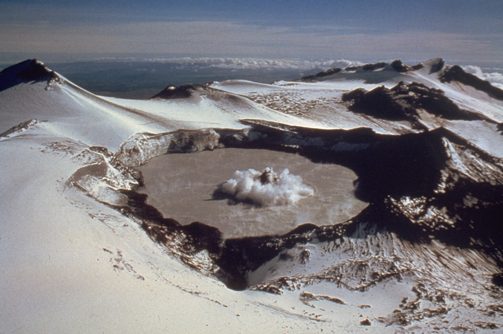 A small phreatic eruption on 29 February 1980, produces a column of ash and steam above Ruapehu's Crater Lake. A darker center plume is surrounded by a white ring produced by pyroclastic surges traveling across the lake surface. This view is from the NW, with Mitre Peak at the upper left. A series of small phreatic explosions had begun on 5 December 1979 and lasted until 15 April the following year. Photo by Peter Otway, 1980 (New Zealand Geological Survey).