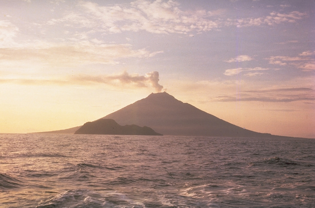 The small, 1.4 x 1.7 Boisa Island is seen here in the foreground from the west with steaming Manam volcano in the distance. Boisa consists of a cone with a summit crater open to the N, and a rim extending to the E coast. The crater of the topographically indistinct stratovolcano is filled by two steep-sided lava domes, the largest of which (left) forms the high point of the island.  Photo by Tony Taylor, 1963 (courtesy of Wally Johnson, Australia Bureau of Mineral Resources).