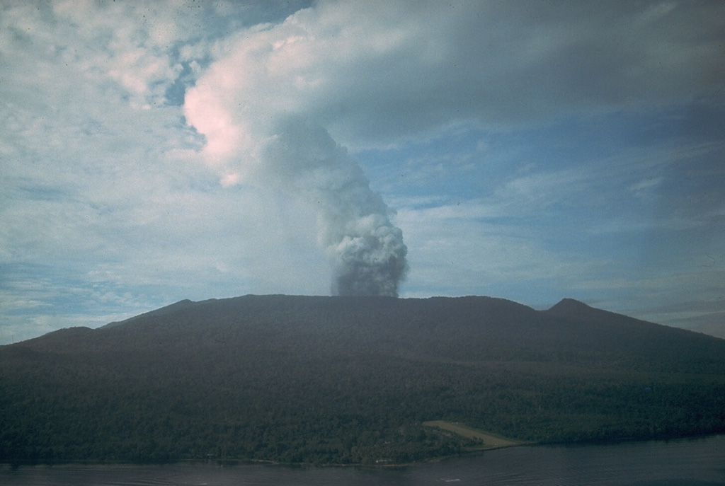 An ash plume rises above the summit of Karkar volcano in 1979. There are two nested summit calderas at the summit of the forested volcano resulting in a broad, low profile. The 5.5-km-wide outer caldera was formed during one or more eruptions, the last of which occurred 9,000 years ago. The 3.2-km-wide inner caldera was formed sometime between 1,500 and 800 years ago. Most historical eruptions, like this one in 1979, have originated from Bagiai cone within the 300-m-deep inner caldera. Photo by Wally Johnson, 1979 (Australia Bureau of Mineral Resources).