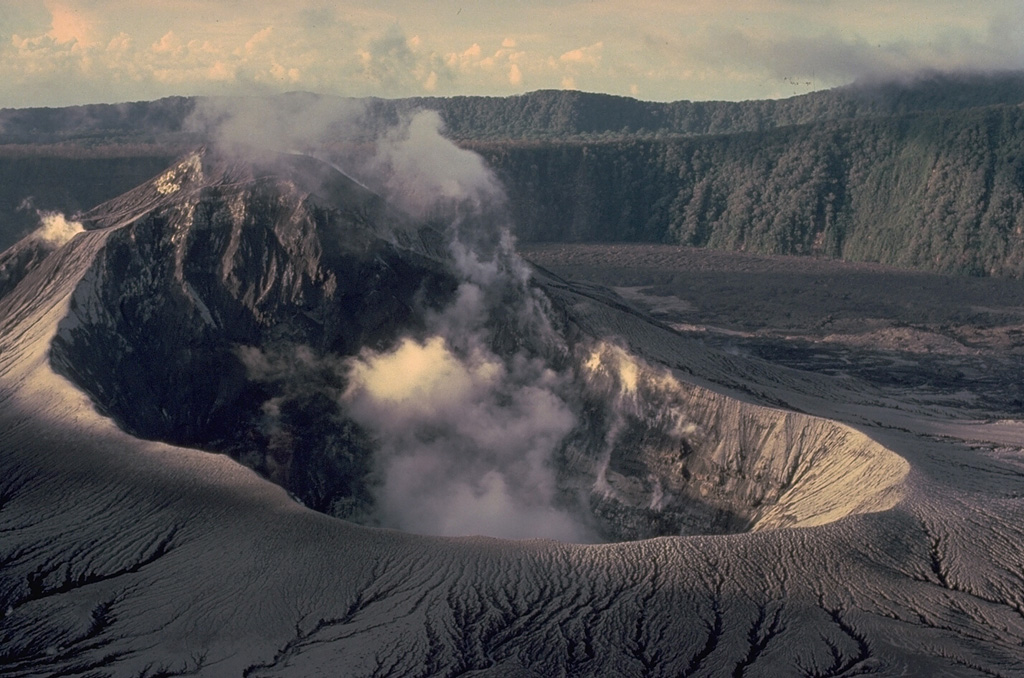 Steam rises from the summit crater of Bagiai cone in the inner caldera of Karkar volcano in September 1979, shortly after an eruption that ended in August.  Fresh pyroclastic-fall deposits that mantle the slopes of the cone originated from a new vent on the caldera floor at the SE base of Bagiai.  This view from the south caldera rim looks across Bagiai cone to the wall of the inner caldera.  The outer caldera wall forms the horizon. Copyrighted photo by Katia and Maurice Krafft, 1979.