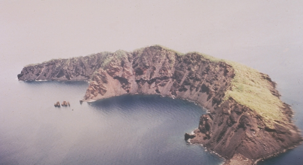 This arcuate, 1.9-km-long, 200-m-wide island is what remains of Ritter Island after its collapse in 1888. Prior to 1888 this was a steep-sided nearly circular island about 780 m high. Large-scale slope failure removed the summit of the conical volcano, leaving an arcuate 140-m-high west-facing scarp, seen here from the SW. Two minor post-collapse explosive eruptions occurred offshore during 1972 and 1974. Photo by Wally Johnson, 1974 (Australia Bureau of Mineral Resources).