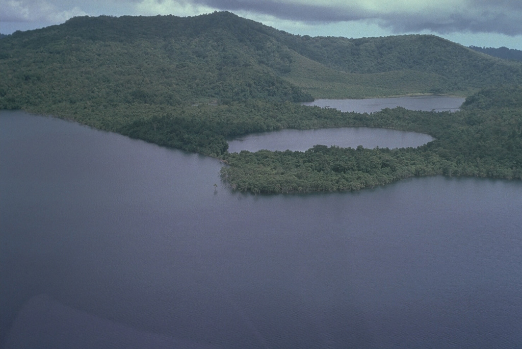 Shown here is the 10.5 x 13.5 km Dakataua caldera at the N tip of the Willaumez Peninsula. Caldera-formatting activity occurred as recently as about 1,150 years ago. A 12-km-wide freshwater lake (foreground), whose surface is only about 50 m above sea level, occupies the caldera. This view from the W shows two maars (right center) and Mount Makalia (top left), which are located along a N-S-trending peninsula. Photo by Russell Blong, 1988 (Macquarie University).