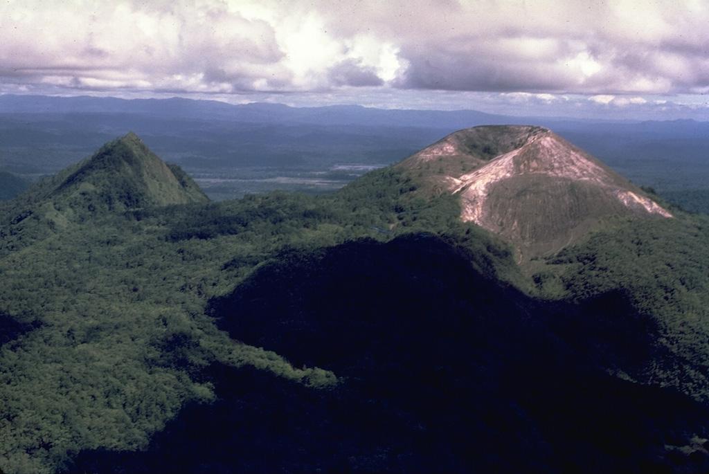 Pago (right), seen here from the N, is a young cone that was constructed within the 5.5 x 7.5 km Witori caldera. Caldera formation occurred about 3,300 years ago and was accompanied by voluminous pyroclastic flows. Pago, which may have formed less than 350 years ago, has grown to a height above the caldera rim. The vegetated lava flow that descends to the left between Pago and the peak to the left was emplaced during a 1911-18 eruption. The 5-km-long lava flow banked against the eastern caldera rim. Photo by Wally Johnson, 1968 (Australia Bureau of Mineral Resources).