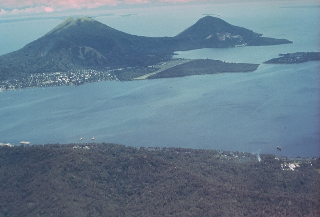 Rabaul caldera and Blanche Bay are seen here from the west. Two pre-caldera cones lie across the bay, Mount Kombiu (known as The Mother) on the left and Mount Turangunan (known as the South Daughter) on the right. Rabaul city lies below Kombiu, and the post-caldera Tavurvur is the partly unvegetated volcano below and to the right of Turangunan. Flat-lying Matupit Island (upper right) has undergone significant uplift during recent periods of caldera unrest. Photo by Russell Blong, 1980 (Macquarie University).