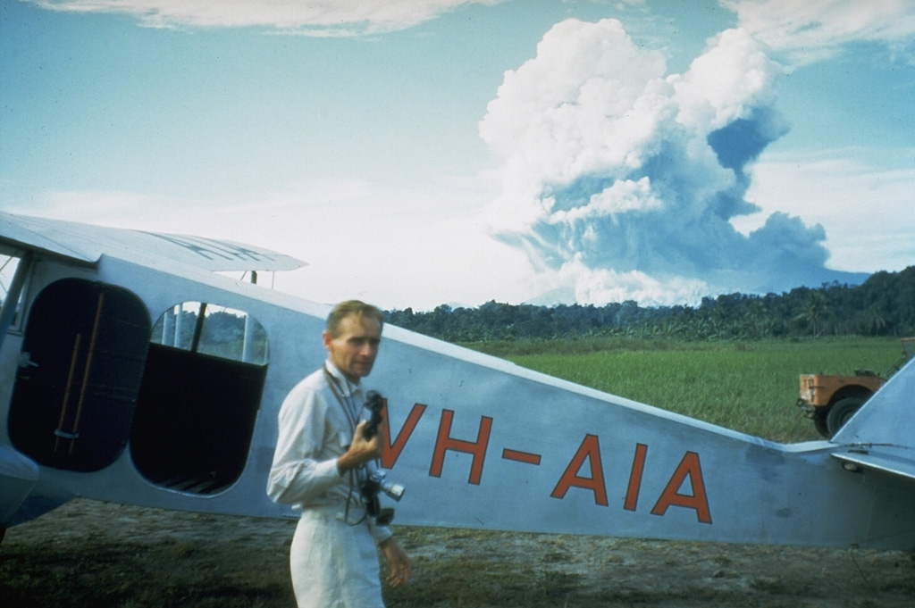 Australian volcanologist Tony Taylor in front of Mount Lamington, which is erupting in the distance on 5 February 1951. Taylor investigated the activity at Lamington through the course of the eruption.  Photo courtesy of Wally Johnson, 1951 (Australia Bureau of Mineral Resources).