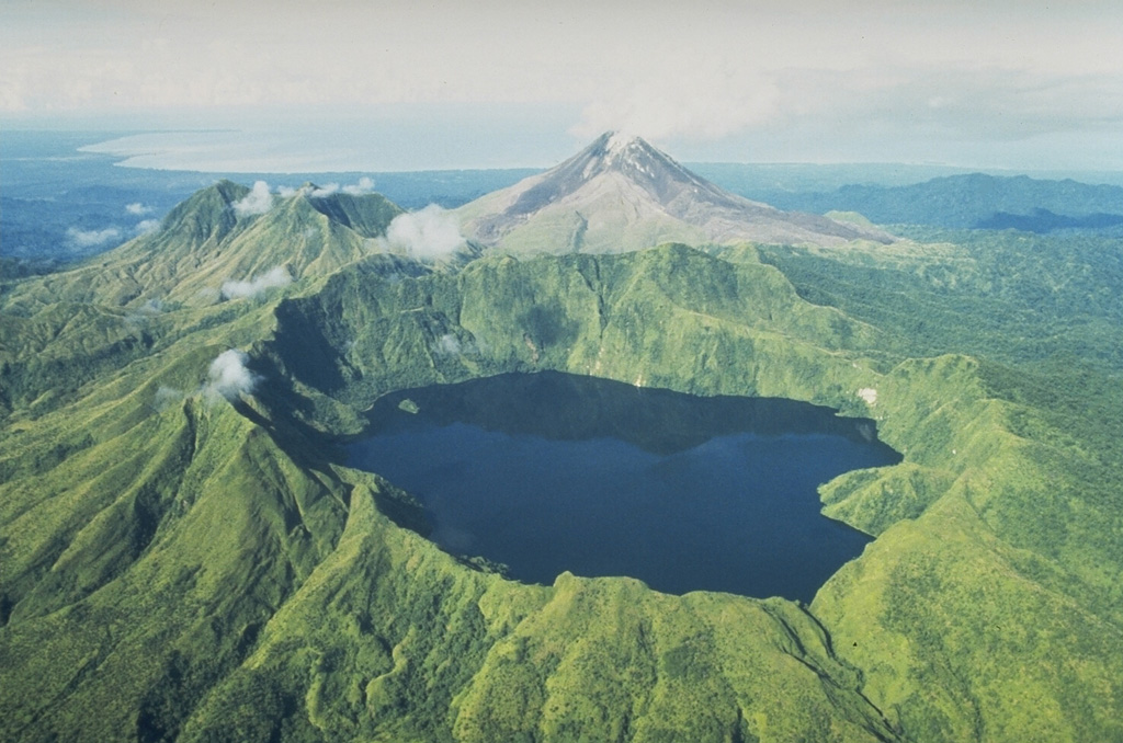 The caldera lake of Billy Mitchell in front of the unvegetated Bagana volcano. The Solomon Sea can be seen in the distance to the SW. Two major explosive eruptions from Billy Mitchell, one about 900 and the other about 370 years ago, produced ashfall that covered most of the N half of Bougainville Island and pyroclastic flow and surge deposits that extend 25 km to the E coast. The younger eruption may have been responsible for formation of the summit caldera. Photo by Wally Johnson, 1988 (Australia Bureau of Mineral Resources).