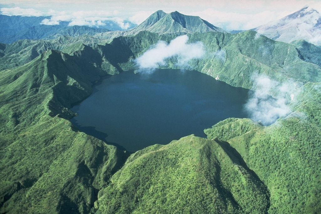 Billy Mitchell truncated by a 2-km-wide caldera containing a lake. It is seen here from the north, with the eroded, forested Reini volcano on the center horizon and neighboring Bagana volcano at the top right. Billy Mitchell has been the source of some of the largest Holocene eruptions of Papua New Guinea. Two major explosive eruptions, one about 900 years ago and the other about 370 years ago, produced ashfall across most of the N half of Bougainville Island. Photo by Wally Johnson, 1989 (Australia Bureau of Mineral Resources).