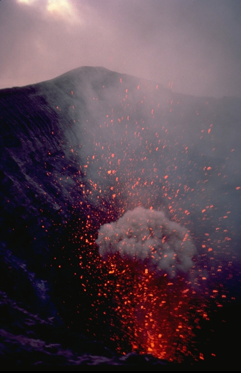 Clots of incandescent magma ejected from a vent on the floor of the summit crater of Yasur volcano rise to the height of the crater rim.  The more-or-less continual low-level eruptive activity of Yasur, which has been occurring since it was first observed by Captain Cook in 1774, has drawn visitors to the island of Tanna.  Mild strombolian eruptions are occasionally punctuated by more violent explosions. Copyrighted photo by André Demaison, 1982 (courtesy of Katia and Maurice Krafft).