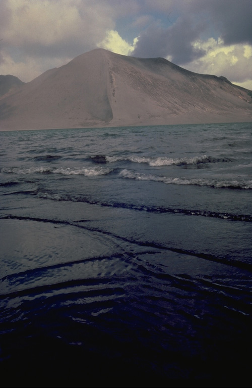 Yasur, the best-known and most frequently visited of the Vanuatu volcanoes, has been in more-or-less continuous strombolian activity since Captain Cook observed ash eruptions in 1774.  This style of activity may have continued for the past 800 years.  Yasur is seen here from the west across windswept Lake Siwi.  Frequent ash ejection has kept the 361-m-high pyroclastic cone mostly unvegetated. Copyrighted photo by André Demaison, 1982 (courtesy of Katia and Maurice Krafft).