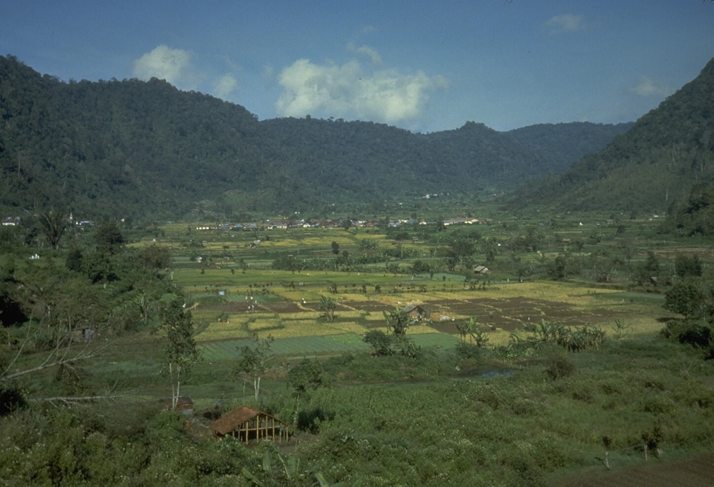 The ridge in the background of this photo is part of the wall of a caldera that contains Sibayak and Pinto volcanoes. The lower slope of Sibayak rises at the far right above the caldera floor, which is occupied by villages and agricultural land. Photo by Tom Casadevall, 1987 (U.S. Geological Survey).