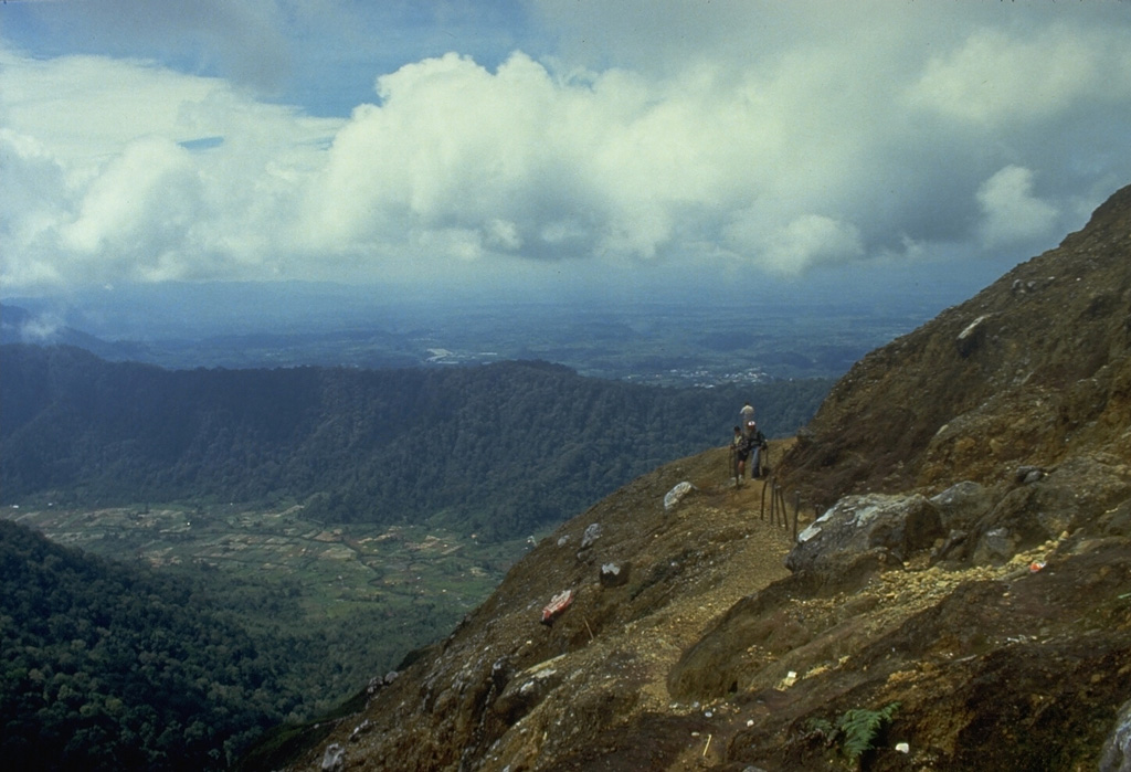 Climbers along a path near the summit of Sibayak volcano. The horizontal forested ridge in the center background, forming part of the southern caldera wall of Singkut, is viewed from an area of hydrothermally altered rock near the summit. Photo by Tom Casadevall, 1987 (U.S. Geological Survey).