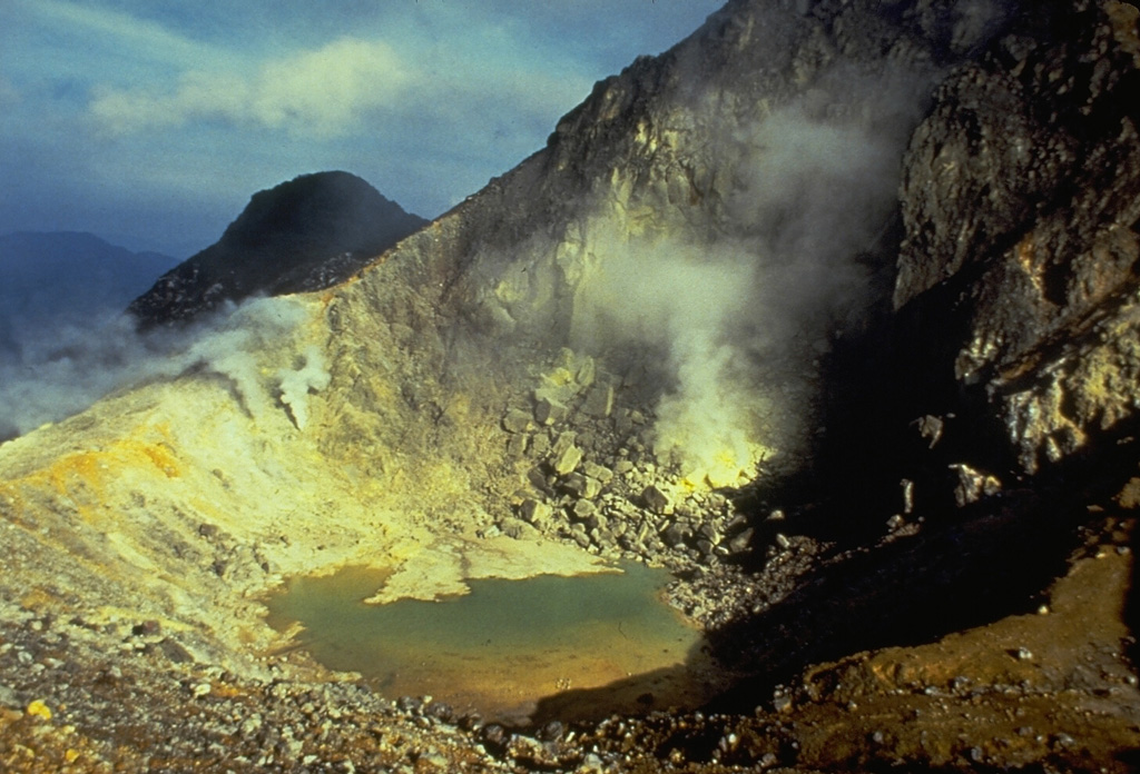 A 300-m-wide crater near the summit of Sibayak volcano contains a small turquoise-colored crater lake and areas of extensive hydrothermal alteration and sulfur mineralization. Plumes rise above active fumaroles at several locations along the far crater wall. Photo by Tom Casadevall, 1987 (U.S. Geological Survey).