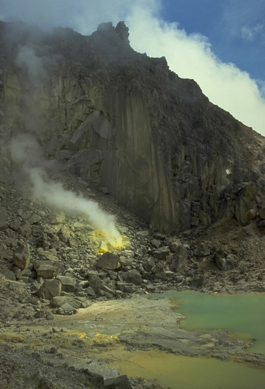 A crater containing a small turquoise-colored lake and active sulfur-coated fumaroles on the summit lava dome of Sibayak volcano. The volcano is considered to be the abode of Nini Kertah Ernala ("Grandmother of the Gleaming Sulfur"), the mountain's spirit. Photo by Tom Casadevall, 1987 (U.S. Geological Survey).