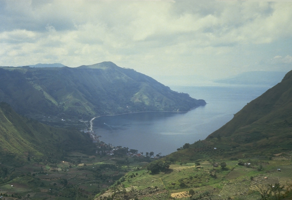 The northern wall of Toba caldera rises about 500 m above the village of Haranggoal. Samosir Island, visible in the distance across Lake Toba on the right, is part of an uplifted block of caldera-fill deposits from the last major eruption of Toba about 74,000 years ago. Photo by Tom Casadevall, 1987 (U.S. Geological Survey)